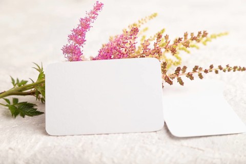 White paper business card mockup with purple astilbe flowers on gray concrete background. Blank,