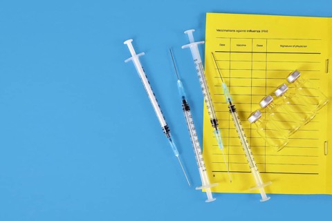 Vaccination concept with vaccine passport, 4 syringes and vials on blue background with copy space