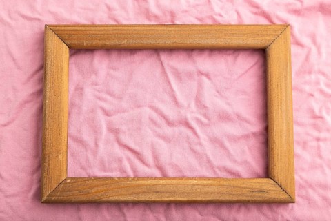 Wooden frame on pink cotton tissue. Top view, flat lay, natural textile background and texture