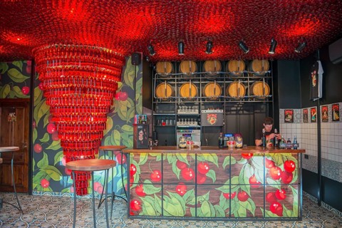 A modern bar with red lighting and barrels in the background, with a bartender behind the counter,