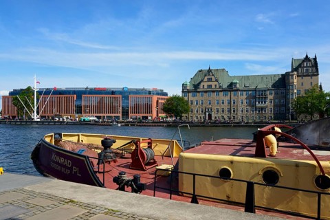 On a sunny day a boat is moored on the river in front of a city scenery with buildings, customs