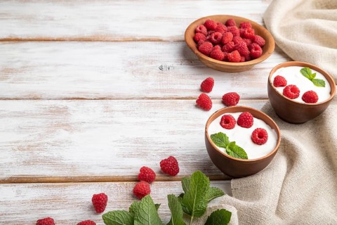 Yogurt with raspberry in clay cups on white wooden background and linen textile. Side view, copy