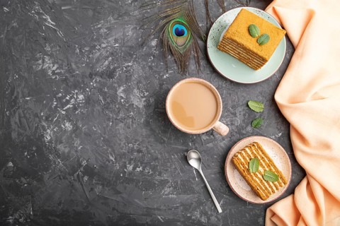 Homemade honey cake with milk cream and mint with cup of coffee on a black concrete background and