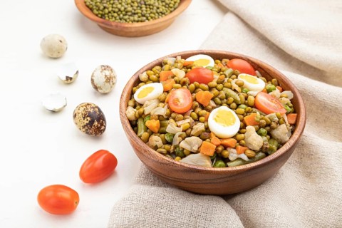 Mung bean porridge with quail eggs, tomatoes and microgreen sprouts on a white wooden background