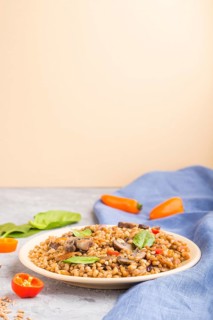 Spelt (dinkel wheat) porridge with vegetables and mushrooms on ceramic plate on gray and orange