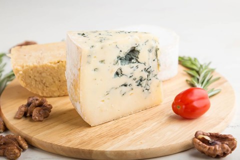 Blue cheese and various types of cheese with rosemary and tomatoes on wooden board on a white