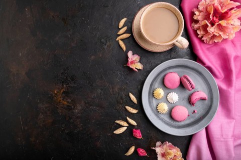 Purple macarons or macaroons cakes with cup of coffee on a black concrete background and pink