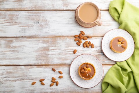 Sweet tartlets with almonds and caramel cream with cup of coffee on a white wooden background and