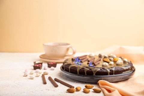 Homemade chocolate brownie cake with caramel cream and almonds with cup of coffee on a white and