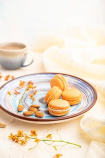 Orange macarons or macaroons cakes with cup of coffee on a white concrete background and linen
