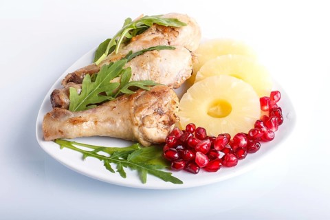 Fried chicken legs with rucola, pineapple and pomegranate seeds isolated on white background, close