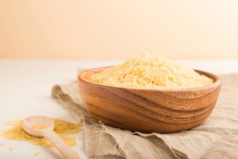 Wooden bowl with raw golden rice and wooden spoon on a white wooden background and linen textile.