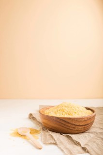 Wooden bowl with raw golden rice and wooden spoon on a white and orange background and linen