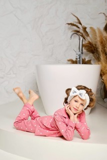 Smiling young girl laying down relaxed on the floor in the bathroom, wearing a cozy pink pajama and