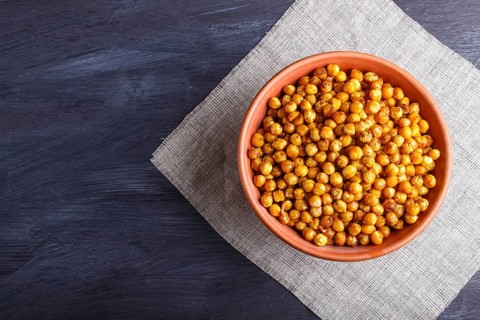 Fried chickpeas with spices in a clay plate on black wooden background, top view, copy space
