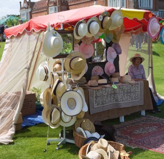 Woman selling hats from tent stall during garden event at Helmingham Hall, Suffolk, England, United