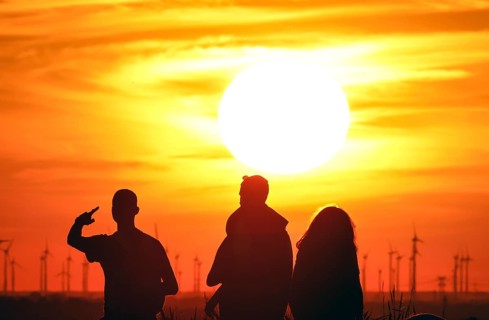 People on Berlin's Drachenberg at sunset. A wind farm near Nauen in Brandenburg can be seen in the
