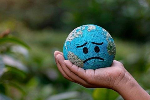 Small planet earth globe with sad face held by hand. Generative Ai, AI generated