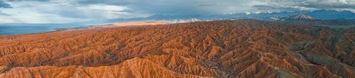 Panorama, landscape of eroded hills, badlands at sunset, behind mountain peaks of the Tian Shan