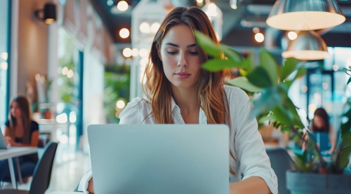 A business woman is sitting at a table with a laptop in front of her working remotely with the team