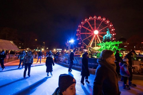 Ice skaters in front of the Neptune Fountain and a Ferris wheel at the Christmas market on
