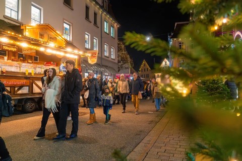 People stroll through an illuminated Christmas market, surrounded by festive stalls and a cheerful