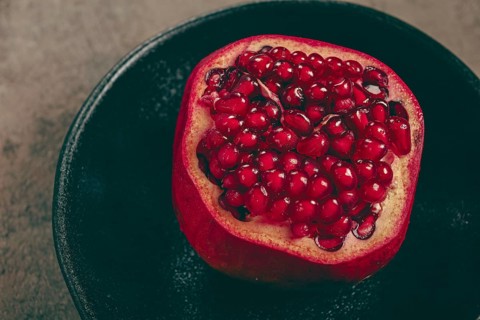 Sliced fresh pomegranate, on a black plate, top view, rustic style, no people