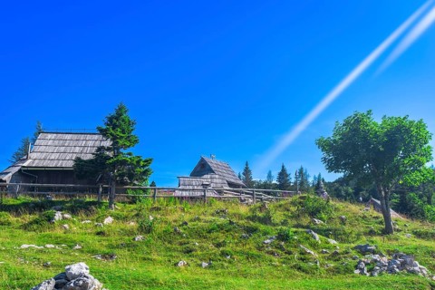 Scenic view of idyllic wooden huts on velika planina plateau with lush green meadows and clear blue