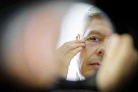 Symbolic photo on the subject of eye wrinkles. A man looks at his eye wrinkles in the mirror.
