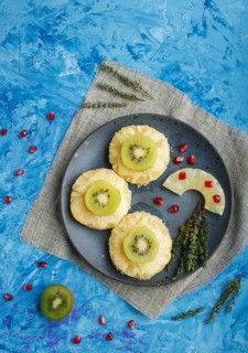 Pieces of baked pork with pineapple, cheese and kiwi on blue background, top view, copy space