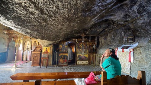 Interior view of a church with a woman praying on a wooden bench and religious art, rock grotto,