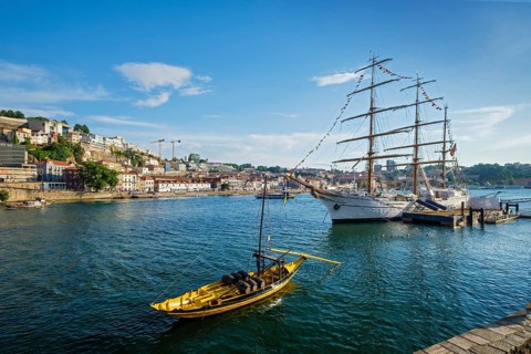 View of Vila Nova de Gaia city with sailing ship and traditional boat with port wine barrels and