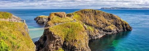 Cliff landscape with bridge and turquoise water under a blue sky, Carrick Bridge