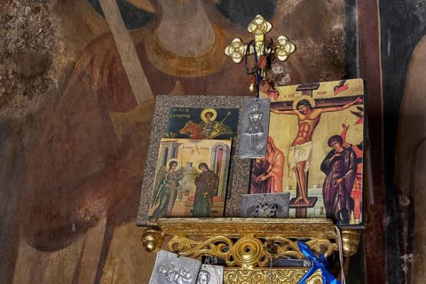 Close-up of an altar with icons and a crucifixion symbol in a church, wall paintings are visible in