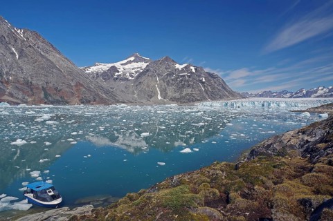 A small boat moored on a clear fjord in front of an impressive mountain and glacier landscape, Knud