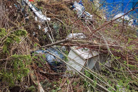 Pile of discarded cut and sawed deciduous and coniferous tree branches, plastic bags and wooden