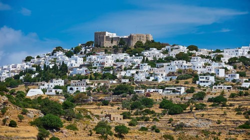Whitewashed houses nestle against a green hill crowned by a castle under a blue sky, Monastery of