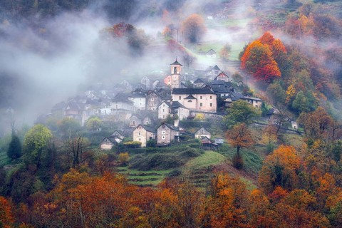Village view of Corippo in the fog surrounded by autumn-coloured deciduous trees, Verzasca Valley,