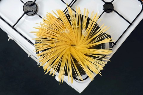 Top view of a pot with boiling water on the stove, with uncooked spaghetti noodles placed upright.