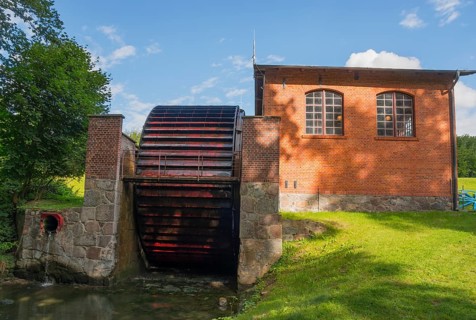 A large waterwheel next to a brick building in a green setting, engine house with waterwheel to