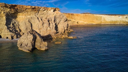 Dramatic cliff landscape with calm blue water, drone shot, evening light, Araki Beach, southwest