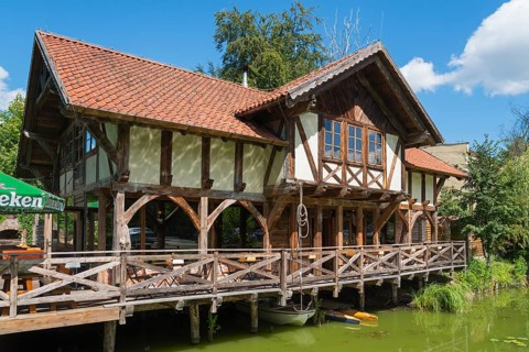 Half-timbered house with terrace by the water, surrounded by green nature and blue sky, Restaurant