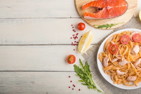 Semolina pasta with salmon and salmon steak on a white wooden background and linen textile. Top
