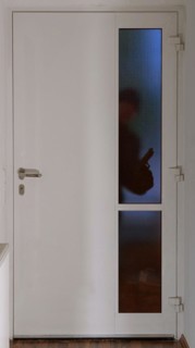 A burglar stands in front of an entrance door in the dark with a gun and looks through the glass
