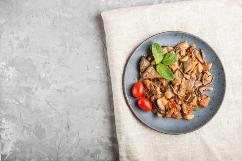 Fried oyster mushrooms with tomatoes on gray concrete background. Top view, copy space