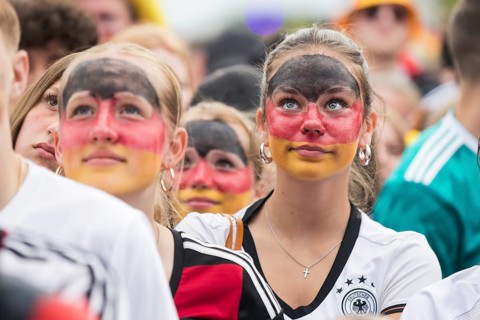 Women wearing make-up in the German national colours watch the football match in the fan zone at