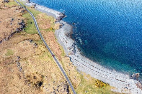 Aerial view of coast at Loch na Keal, coastal road and lonely red car on single track road, Isle of