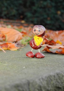 Funny chestnut figure with yellow scarf on a wall in autumn leaves, North Rhine-Westphalia,