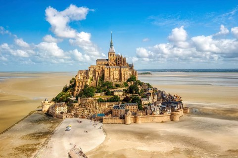 Gothic abbey on a sandy island, surmounted by a tower, in bright daylight, Le Mont-Saint-Michel