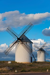 Two white windmills in a landscape under a blue sky and clouds in the background, Campo de